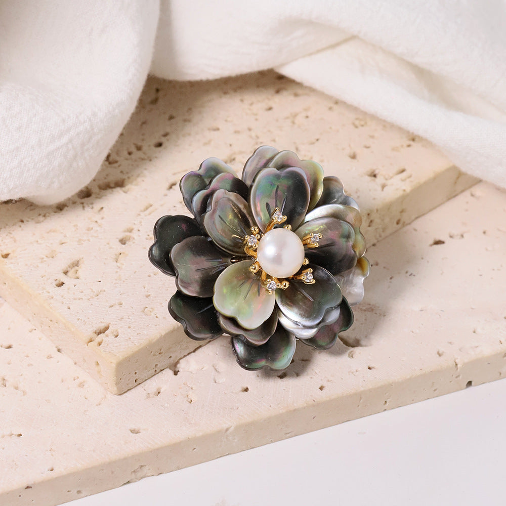 Elegant camellia brooch featuring black mother-of-pearl petals, a central white pearl, and shimmering zirconia accents