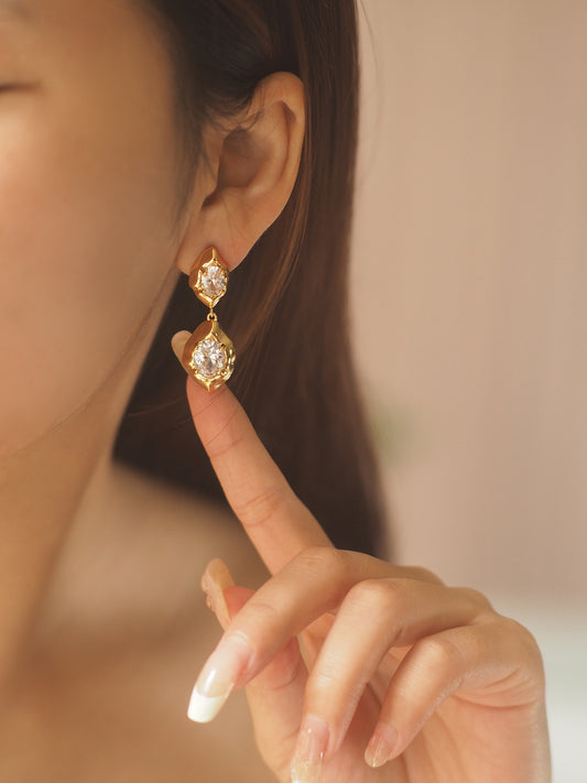 A pair of geometric drop earrings with a hammered gold texture and brilliant oval zircon accents