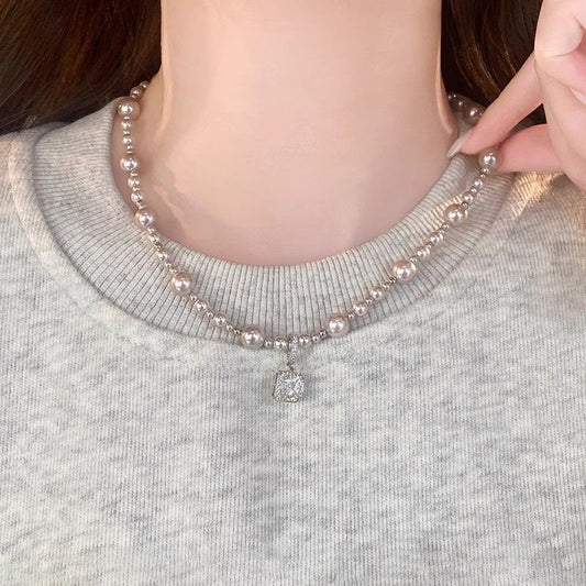 Modern silver-tone necklace featuring a sleek arc pendant with a dangling round pearl and shimmering zircon accents