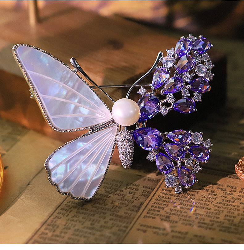 Unique asymmetric butterfly brooch with white mother-of-pearl, purple cubic zirconia clusters, and a central pearl