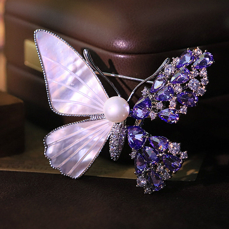 Unique asymmetric butterfly brooch with white mother-of-pearl, purple cubic zirconia clusters, and a central pearl