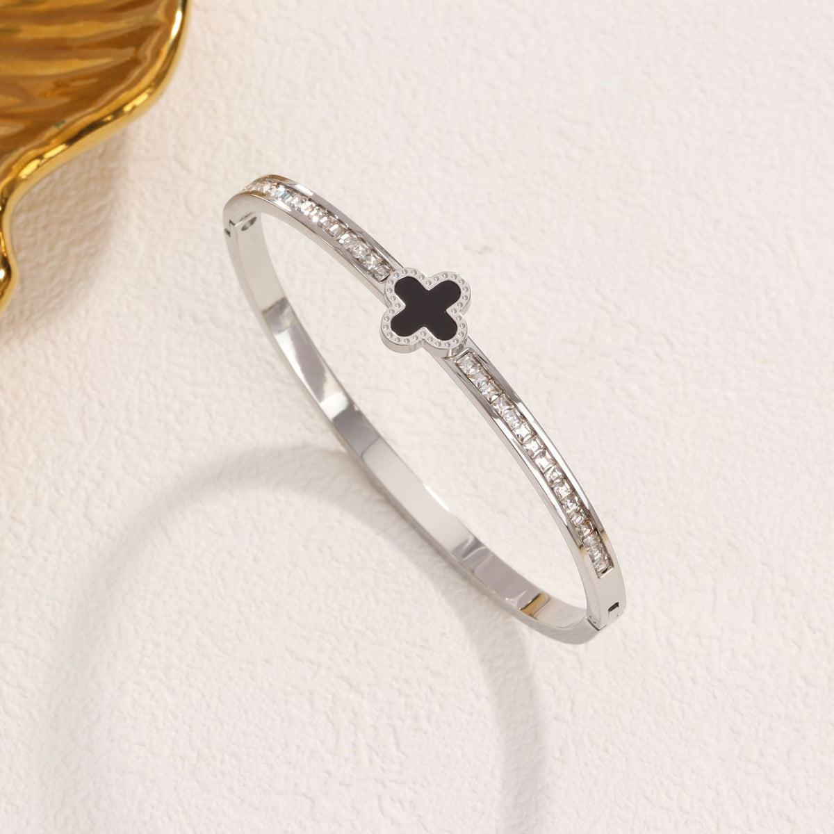 Black enamel clover station and channel-set cubic zirconia hinged cuff bangle in waterproof 18k gold plated stainless steel jewelry.