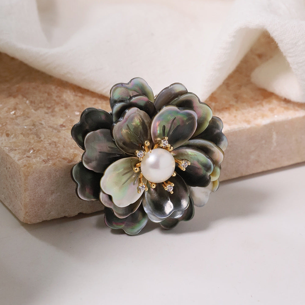 Elegant camellia brooch featuring black mother-of-pearl petals, a central white pearl, and shimmering zirconia accents