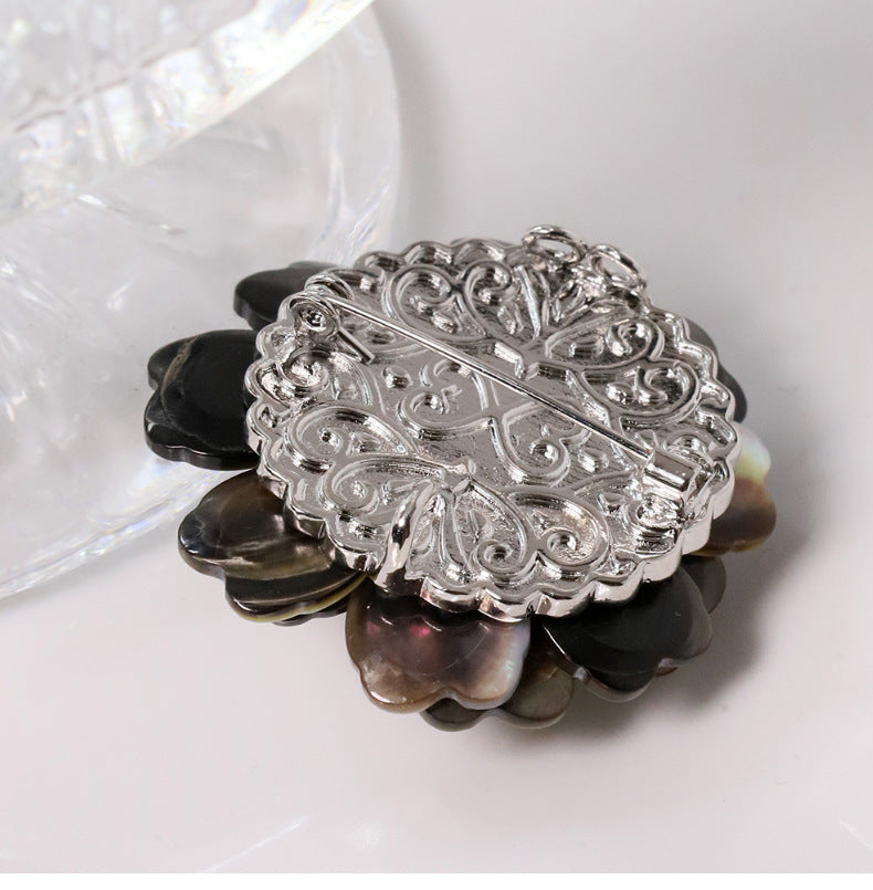 Elegant camellia brooch featuring black mother-of-pearl petals, a central white pearl, and shimmering zirconia accents
