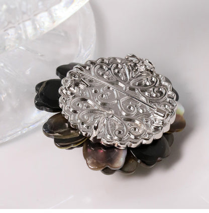 Elegant camellia brooch featuring black mother-of-pearl petals, a central white pearl, and shimmering zirconia accents