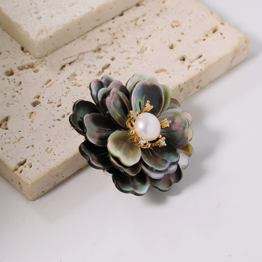 Elegant camellia brooch featuring black mother-of-pearl petals, a central white pearl, and shimmering zirconia accents