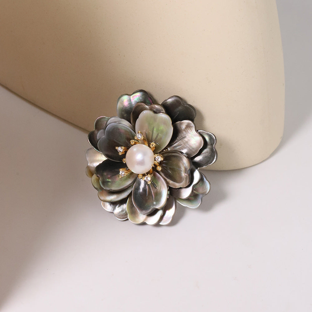 Elegant camellia brooch featuring black mother-of-pearl petals, a central white pearl, and shimmering zirconia accents