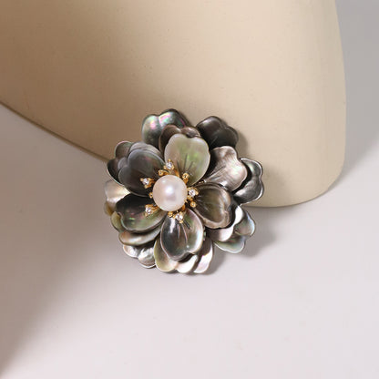 Elegant camellia brooch featuring black mother-of-pearl petals, a central white pearl, and shimmering zirconia accents