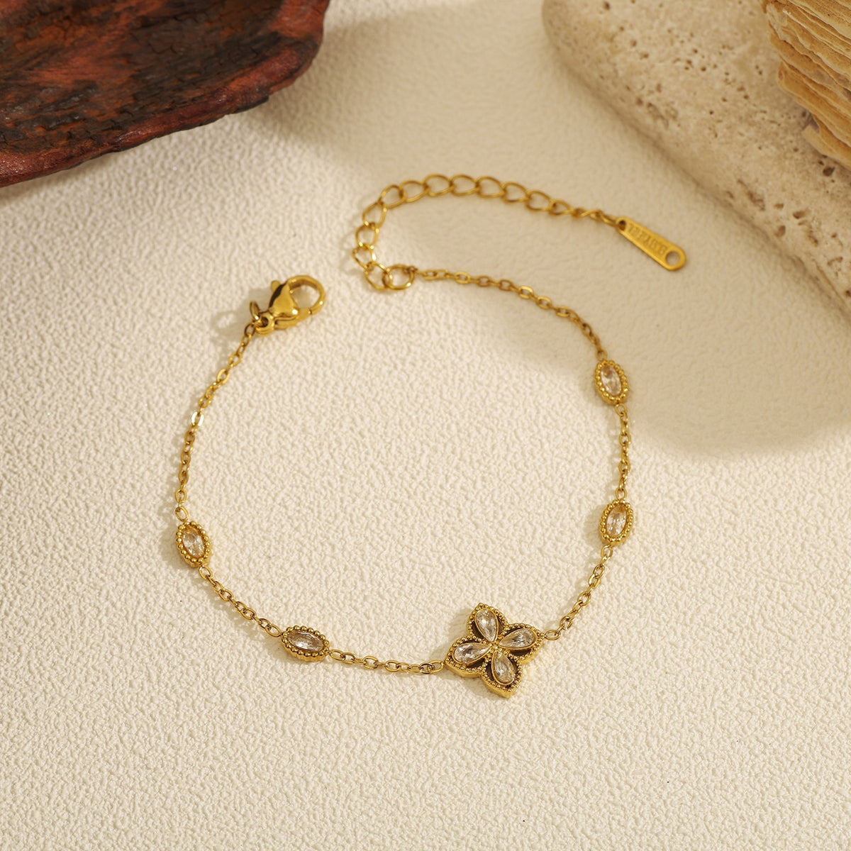 Cubic zirconia cz four petal flower pendant and oval bezel stations cable chain stainless steel jewelry bracelet in waterproof 18k gold plated finish.