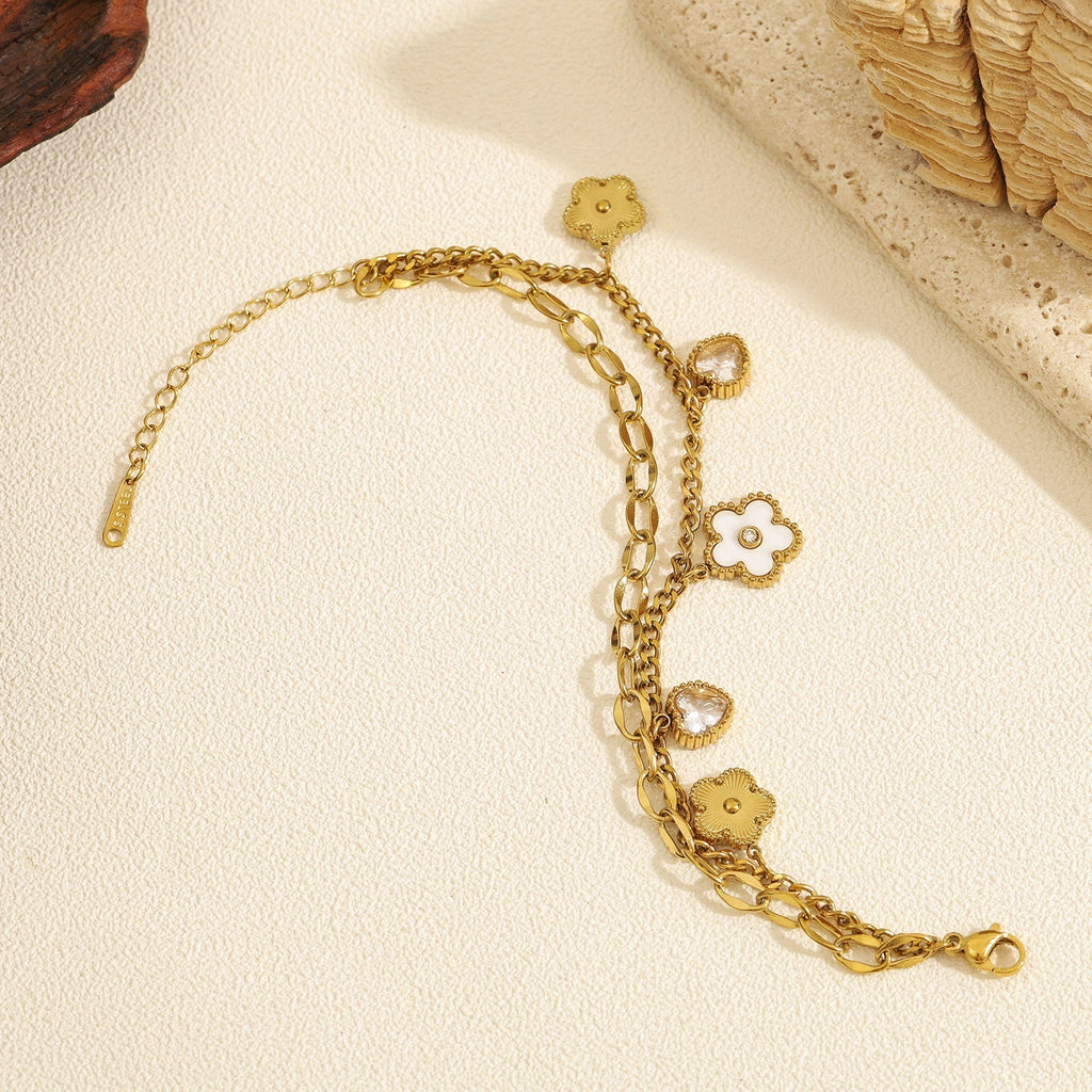 Double layer link chain white shell flower motif and heart cubic zirconia charm stainless steel jewelry bracelet in waterproof 18k gold plated finish.
