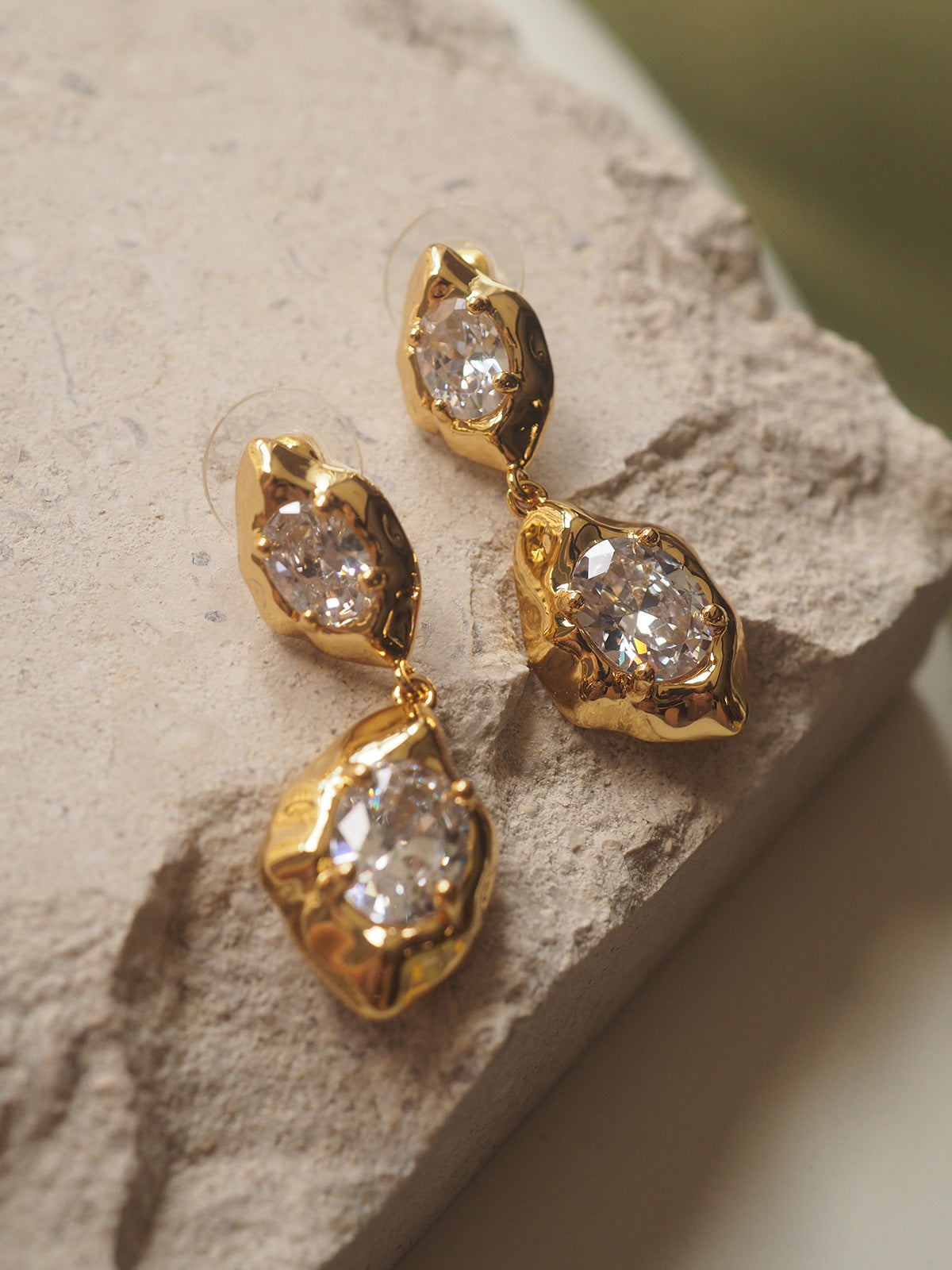 A pair of geometric drop earrings with a hammered gold texture and brilliant oval zircon accents