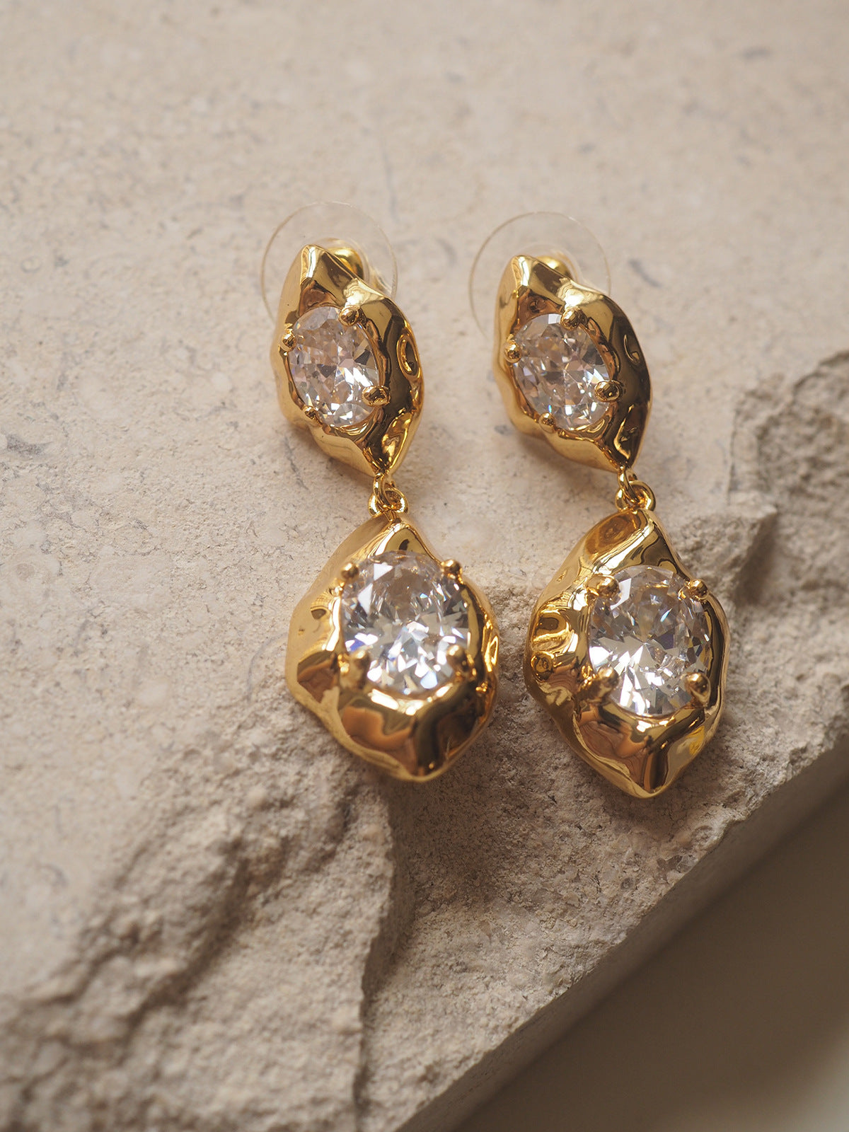 A pair of geometric drop earrings with a hammered gold texture and brilliant oval zircon accents