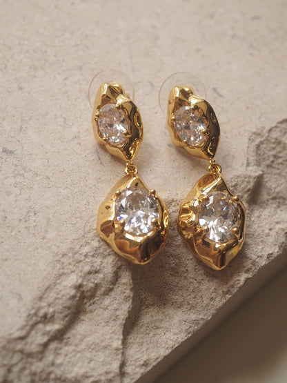 A pair of geometric drop earrings with a hammered gold texture and brilliant oval zircon accents