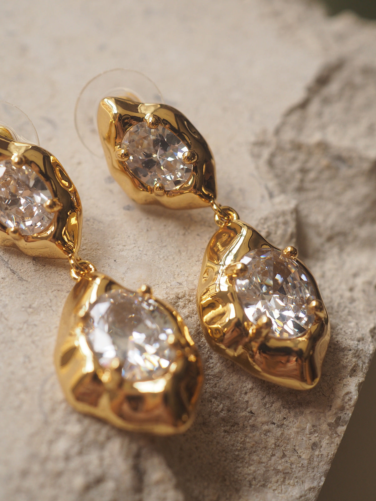 A pair of geometric drop earrings with a hammered gold texture and brilliant oval zircon accents