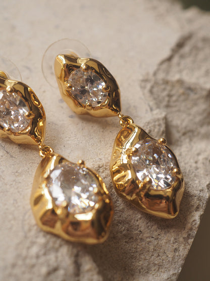 A pair of geometric drop earrings with a hammered gold texture and brilliant oval zircon accents