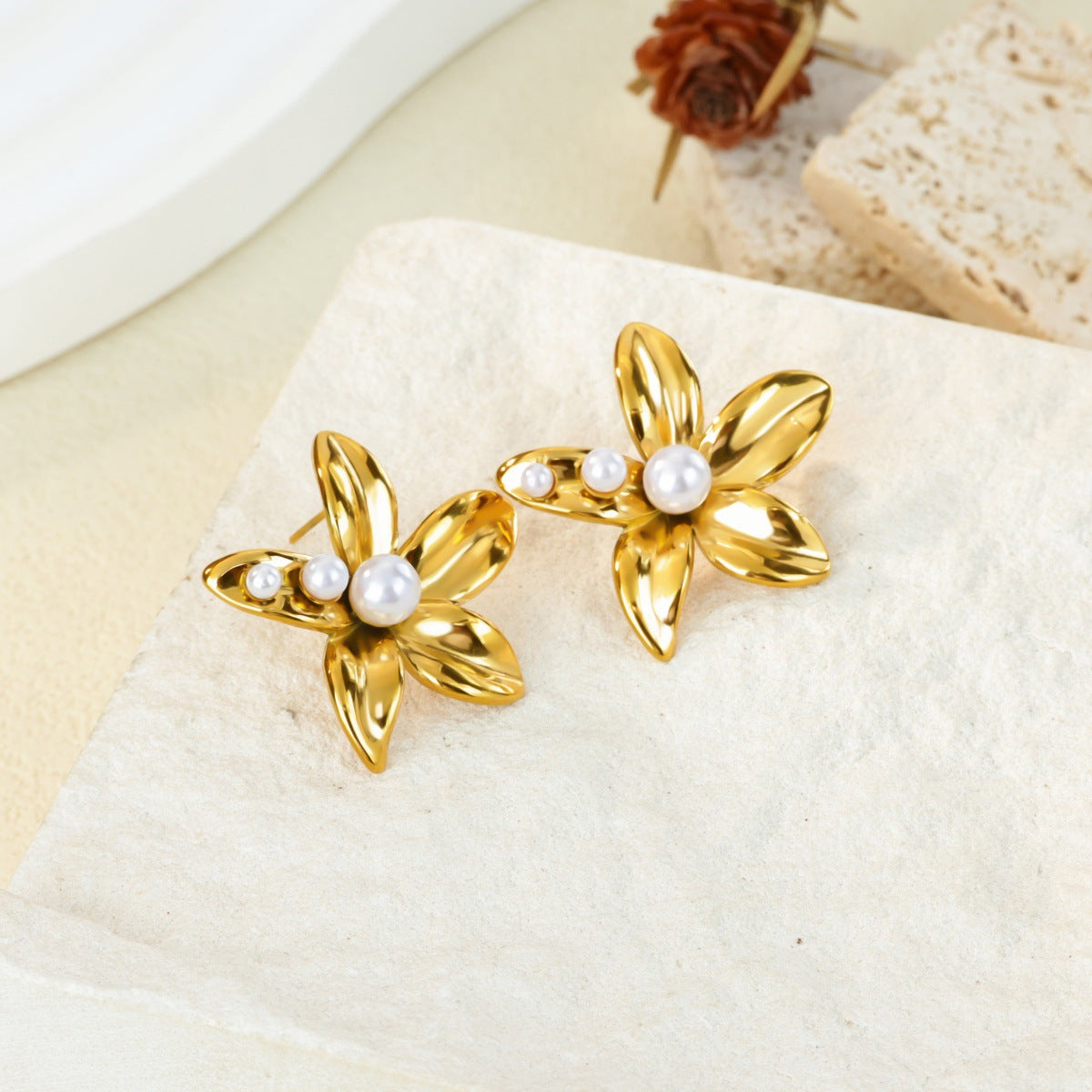 Paired gold flower stud earrings featuring a central white pearl in an elegant blooming petal design