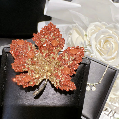 Elegant gold plated maple leaf brooch featuring gradient red cubic zirconia stones in a seasonal autumn design