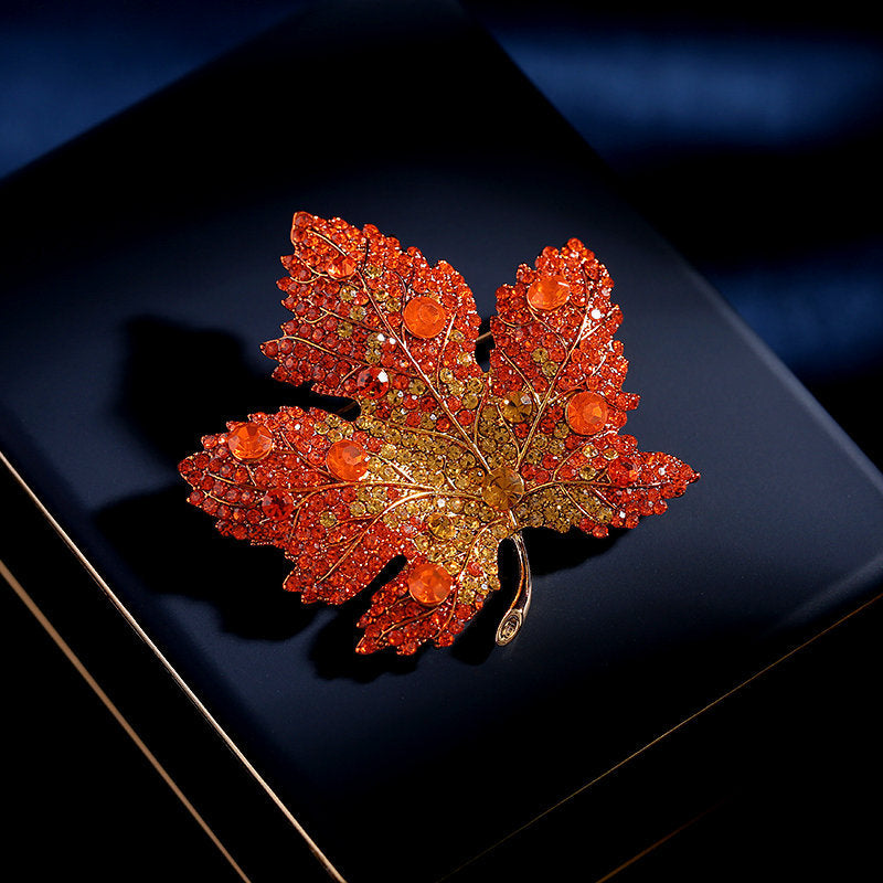 Elegant gold plated maple leaf brooch featuring gradient red cubic zirconia stones in a seasonal autumn design
