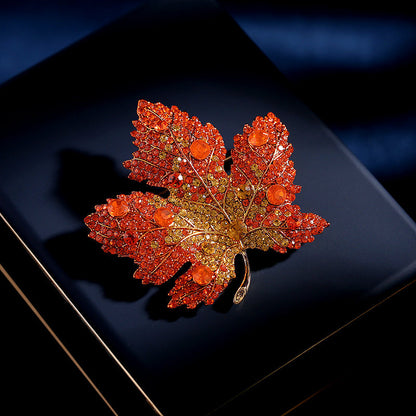 Elegant gold plated maple leaf brooch featuring gradient red cubic zirconia stones in a seasonal autumn design