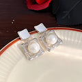 Elegant square zirconia stud earrings with a dangling white pearl charm, available in gold and silver finishe