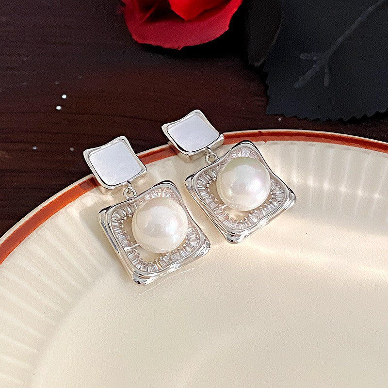 Elegant square zirconia stud earrings with a dangling white pearl charm, available in gold and silver finishe