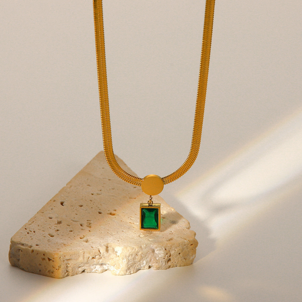 Emerald cut green cubic zirconia cz crystal bezel pendant on flat herringbone snake chain necklace stainless steel jewelry in waterproof 18k gold plated finish.