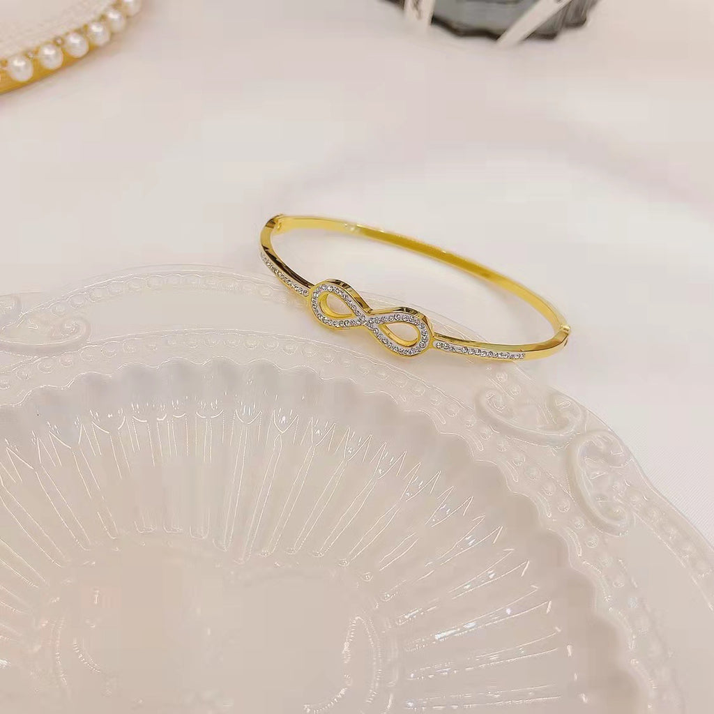 Infinity loop motif pave cubic zirconia accent stainless steel jewelry bangle in waterproof 18k gold plated finish.