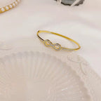 Infinity loop motif pave cubic zirconia accent stainless steel jewelry bangle in waterproof 18k gold plated finish.