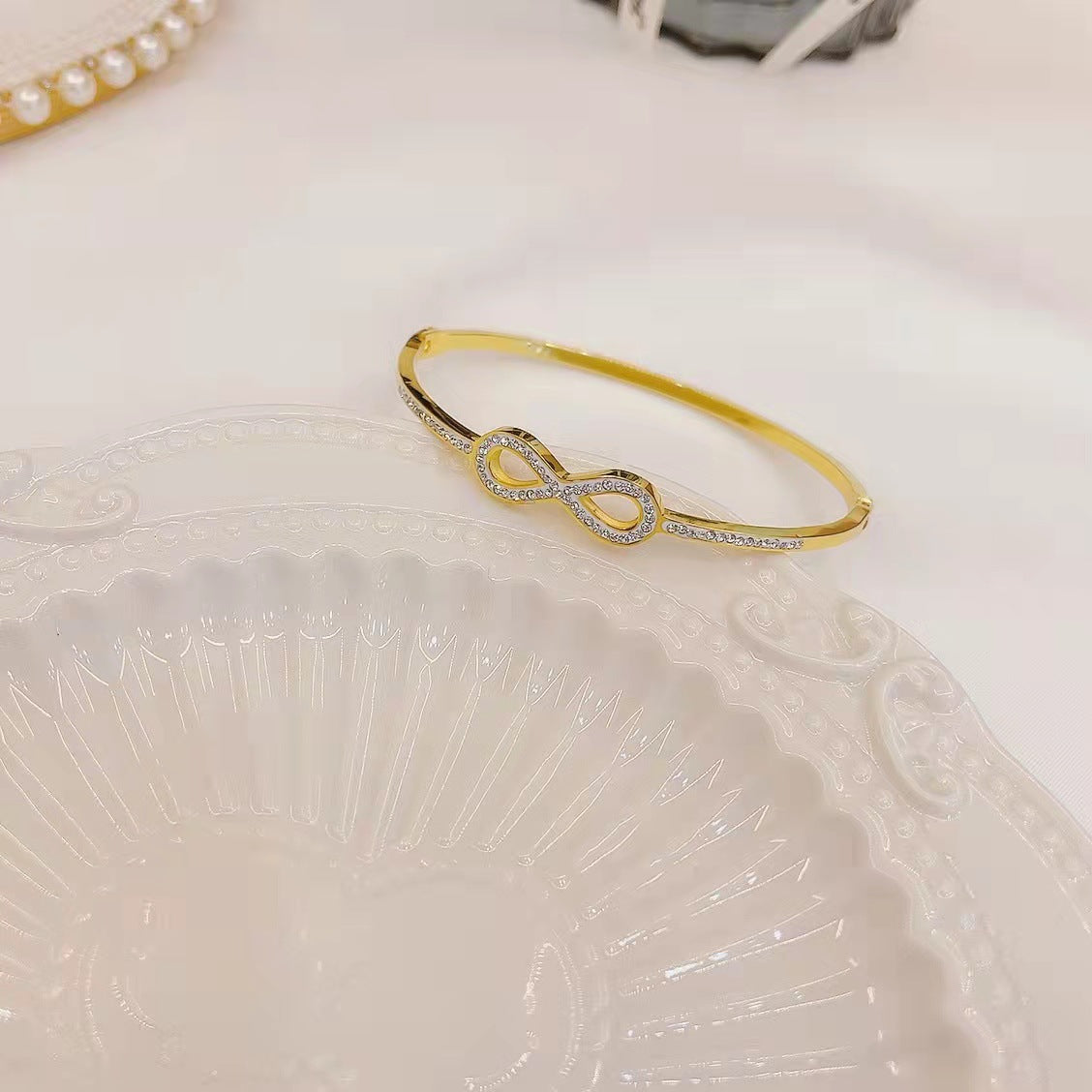Infinity loop motif pave cubic zirconia accent stainless steel jewelry bangle in waterproof 18k gold plated finish.