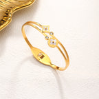 Mother of pearl clover station and crystal accent stainless steel jewelry bangle in waterproof 18k gold plated finish.