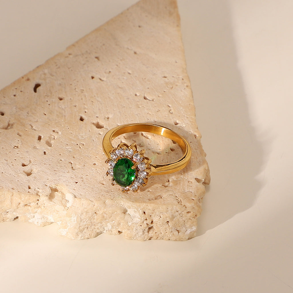 Oval emerald green cubic zirconia center stone framed by a sparkling clear cz crystal halo stainless steel jewelry ring in waterproof 18k gold plated finish.