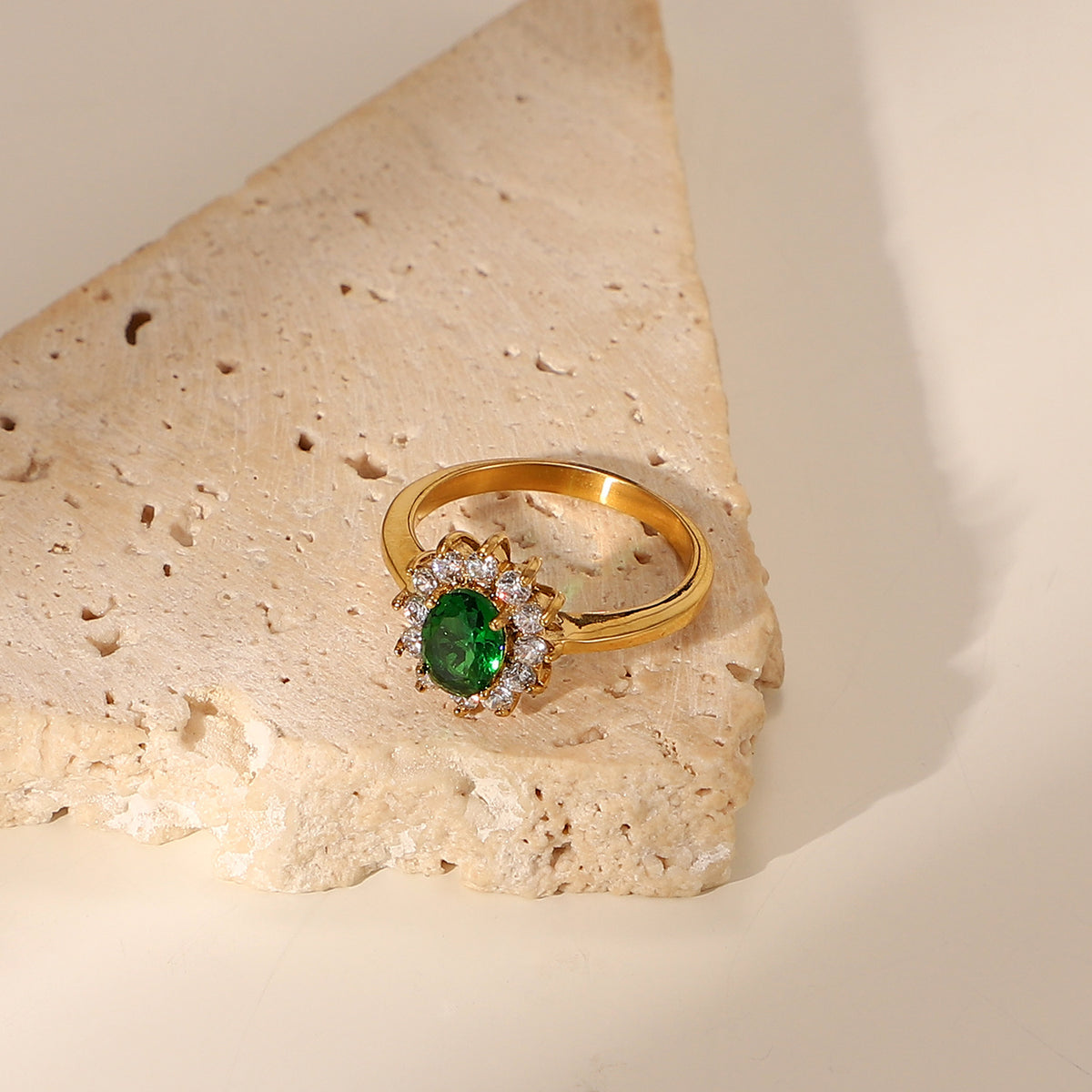 Oval emerald green cubic zirconia center stone framed by a sparkling clear cz crystal halo stainless steel jewelry ring in waterproof 18k gold plated finish.