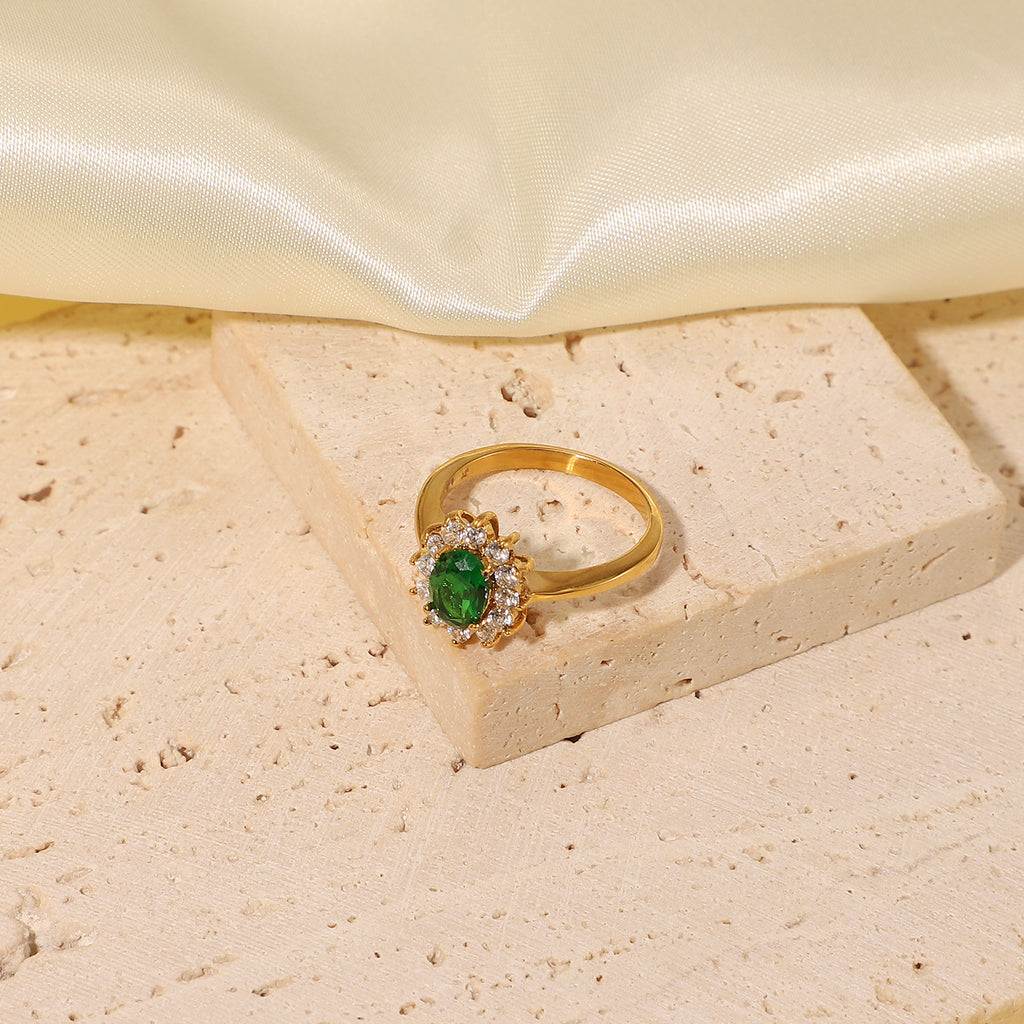 Oval emerald green cubic zirconia center stone framed by a sparkling clear cz crystal halo stainless steel jewelry ring in waterproof 18k gold plated finish.