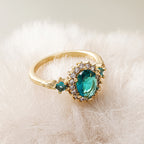 Oval teal blue center stone surrounded by sparkling cubic zirconia cz crystal halo three stone band stainless steel jewelry ring in waterproof 18k gold plated finish.