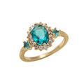 Oval teal blue center stone surrounded by sparkling cubic zirconia cz crystal halo three stone band stainless steel jewelry ring in waterproof 18k gold plated finish.