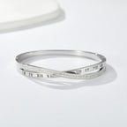 Engraved Roman numeral and pave cubic zirconia crossover stainless steel bangle bracelet jewelry in waterproof 18k gold plated finish.