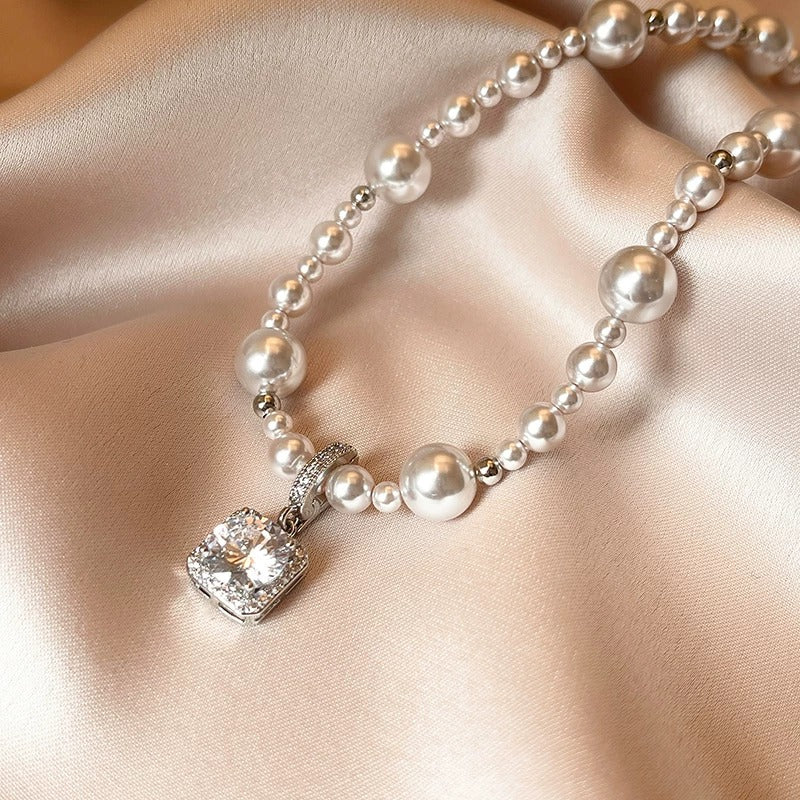 Modern silver-tone necklace featuring a sleek arc pendant with a dangling round pearl and shimmering zircon accents