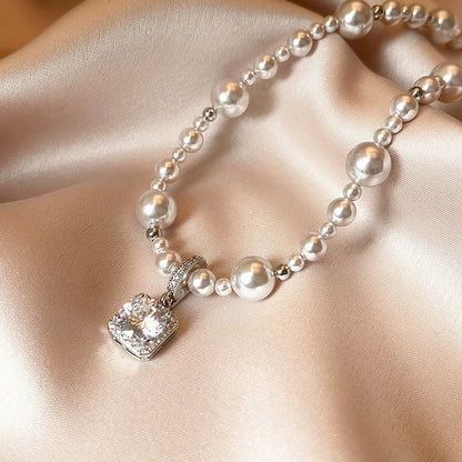 Modern silver-tone necklace featuring a sleek arc pendant with a dangling round pearl and shimmering zircon accents