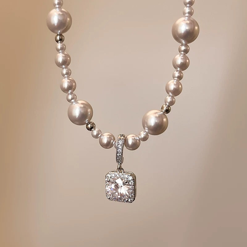 Modern silver-tone necklace featuring a sleek arc pendant with a dangling round pearl and shimmering zircon accents