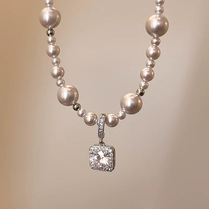 Modern silver-tone necklace featuring a sleek arc pendant with a dangling round pearl and shimmering zircon accents