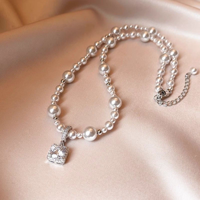 Modern silver-tone necklace featuring a sleek arc pendant with a dangling round pearl and shimmering zircon accents