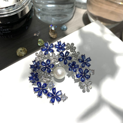 Silver crescent moon brooch featuring blue and white cubic zirconia with a lustrous white pearl accent