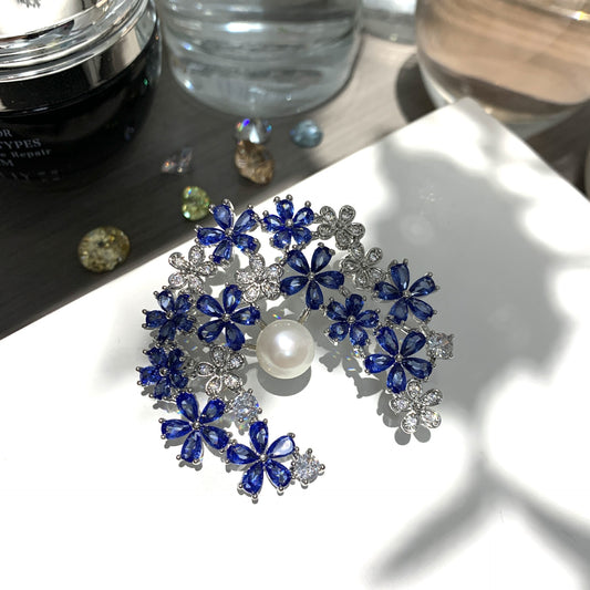 Silver crescent moon brooch featuring blue and white cubic zirconia with a lustrous white pearl accent