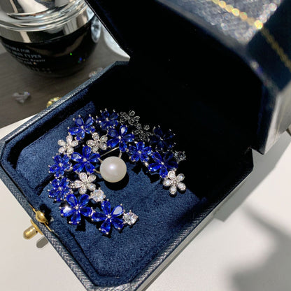 Silver crescent moon brooch featuring blue and white cubic zirconia with a lustrous white pearl accent