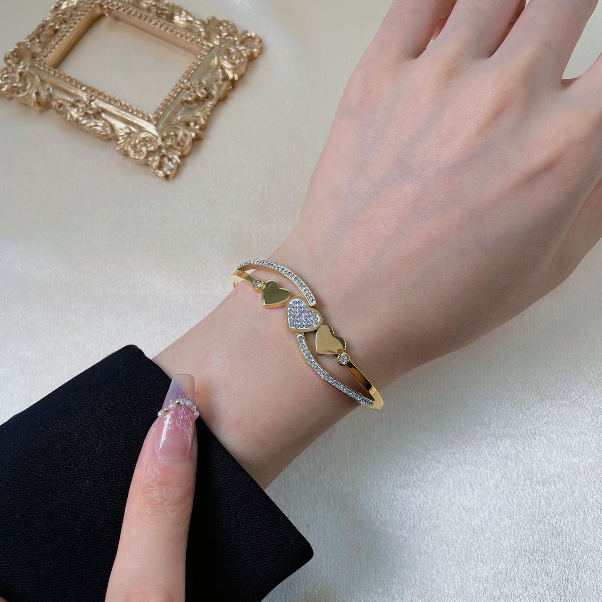 Triple heart station and pave cubic zirconia accent hinged cuff bangle in waterproof 18k gold plated stainless steel jewelry.