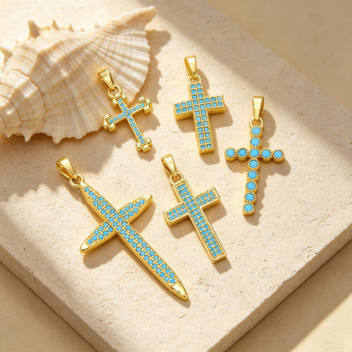 Wholesale stainless steel jewelry collection of gold aqua blue cz cubic zirconia cross pendant charms in various geometric and starburst shapes.